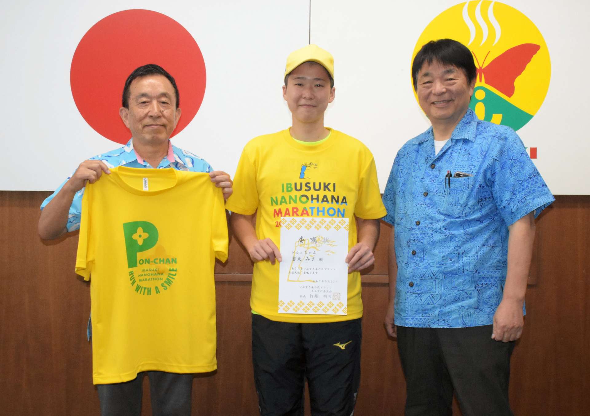 いぶすき菜の花マラソン応援大使の委嘱状とＴシャツを受け取り、笑顔を見せる岩元みささん（中央）＝指宿市役所