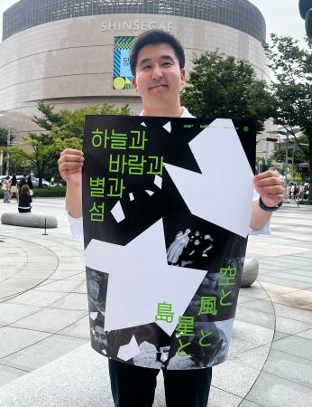　映画「空と風と星と島」のポスターを手にする金明允さん＝１９日、韓国・釜山（共同）