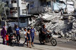 　イスラエルの攻撃で破壊された建物の前を歩くパレスチナの人たち＝４日、パレスチナ自治区ガザ中部ヌセイラト（ロイター＝共同）
