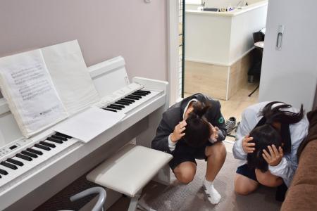 　在宅中に避難訓練の防災行政無線が流れ、両手で頭を守る姿勢でかがむ子どもたち＝１９日午前、石川県輪島市門前町