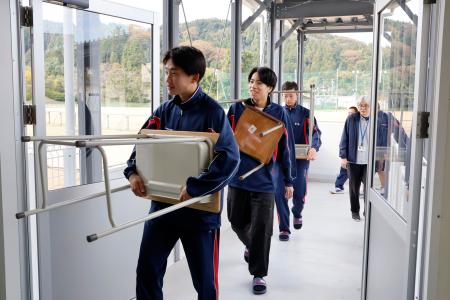 　石川県輪島市の県立門前高で、完成した仮設校舎に勉強机や椅子を運び込む生徒たち＝５日午前