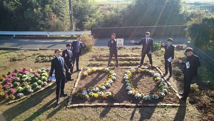新成人の「２０」の形に植えられたビオラの花を囲む山下武文さんの親友７人。遺影を持つのが八重尾塁さん＝２０２０年１月５日、出水市野田町下名（山下ひとみさん提供）