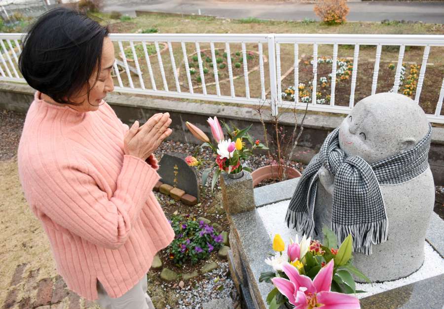 山下武文さんを供養する地蔵に手を合わせる母・ひとみさん。奥の畑には、武文さんが迎えたはずの年齢である「２１」の形に花を植えている＝８日、出水市野田町下名