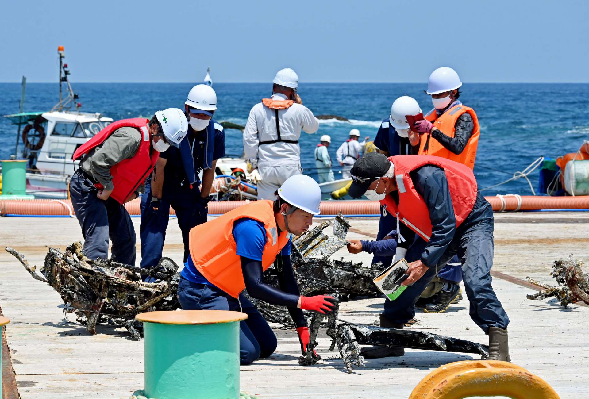 引き揚げられた九七艦攻のものとみられる部材を調べる関係者＝２３日午後、西之表市国上沖