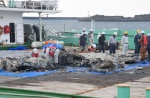台船に引き揚げられた機体の一部を調べる関係者＝２５日、西之表市栄町