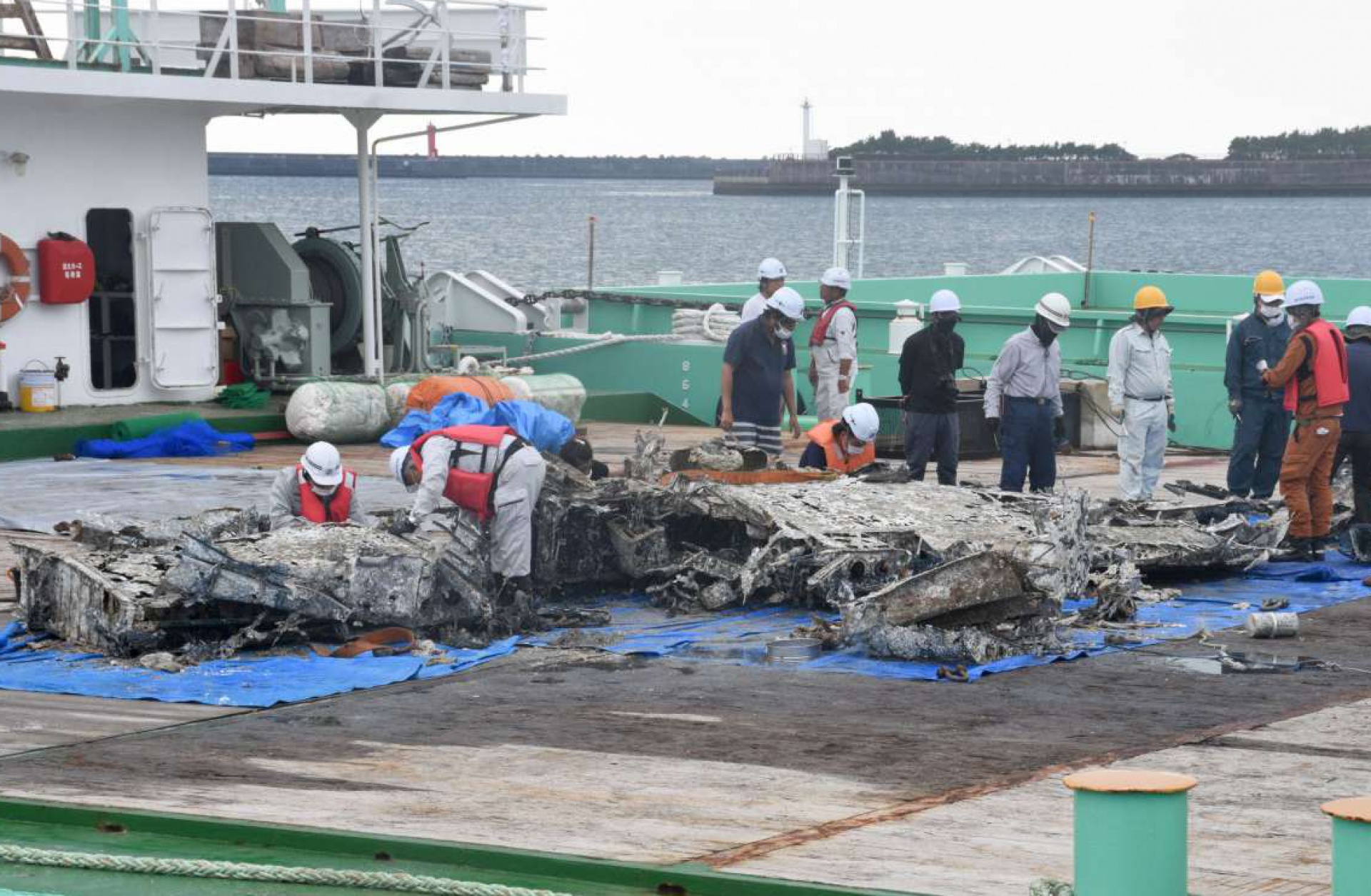 台船に引き揚げられた機体の一部を調べる関係者＝２５日、西之表市栄町
