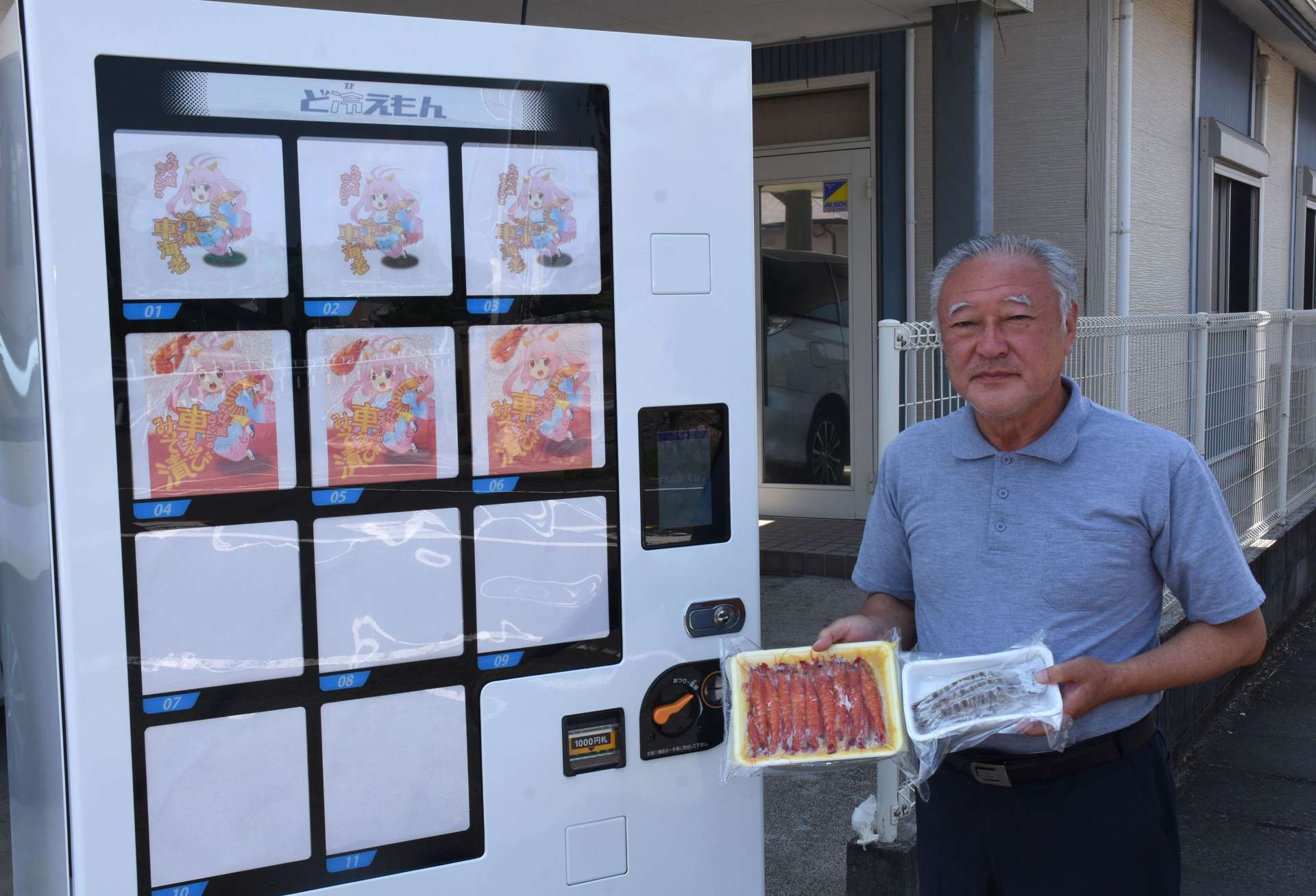 販売を始めた車エビの自動販売機と商品を掲げる中満康蔵社長＝３日、薩摩川内市中郷３丁目のキャピタル
