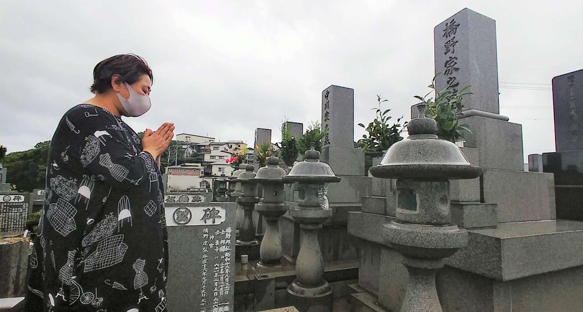 墓前で手を合わせる墓参者。今年は墓守サービスの利用者も多い＝１３日、鹿児島市の唐湊墓地