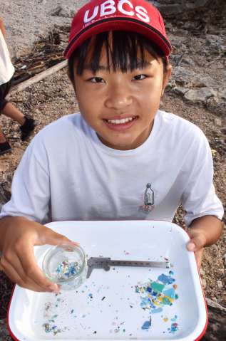 拾い集めたマイクロプラスチックの瓶詰めを手にする竿りりさん