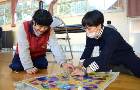 職員と一緒にびょうぶを作る利用者（左）