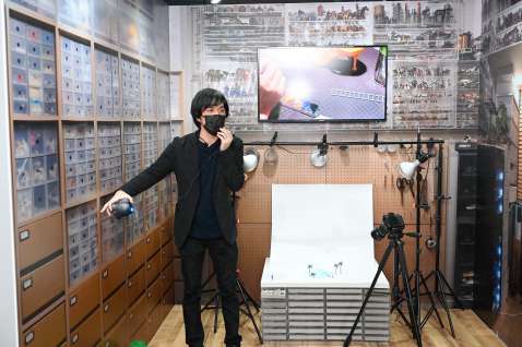 作品展で、撮影機材や人形をしまう棚などアトリエ風景を再現したコーナーに立つ田中達也さん＝1月、鹿児島市のライカ南国ホール