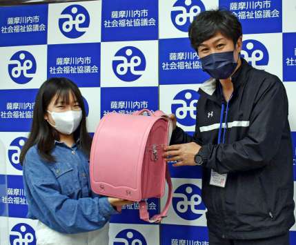 役割を終えたランドセルを山内一宏地域福祉課長（右）に手渡す提供者（薩摩川内市社会福祉協議会提供）