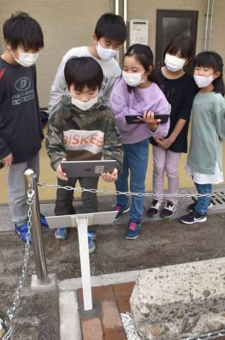 ＱＲコードを読み取る小学生。手前は出土した滑走路跡コンクリート片＝鹿屋市笠之原町のＪＡ直売所どっ菜市場