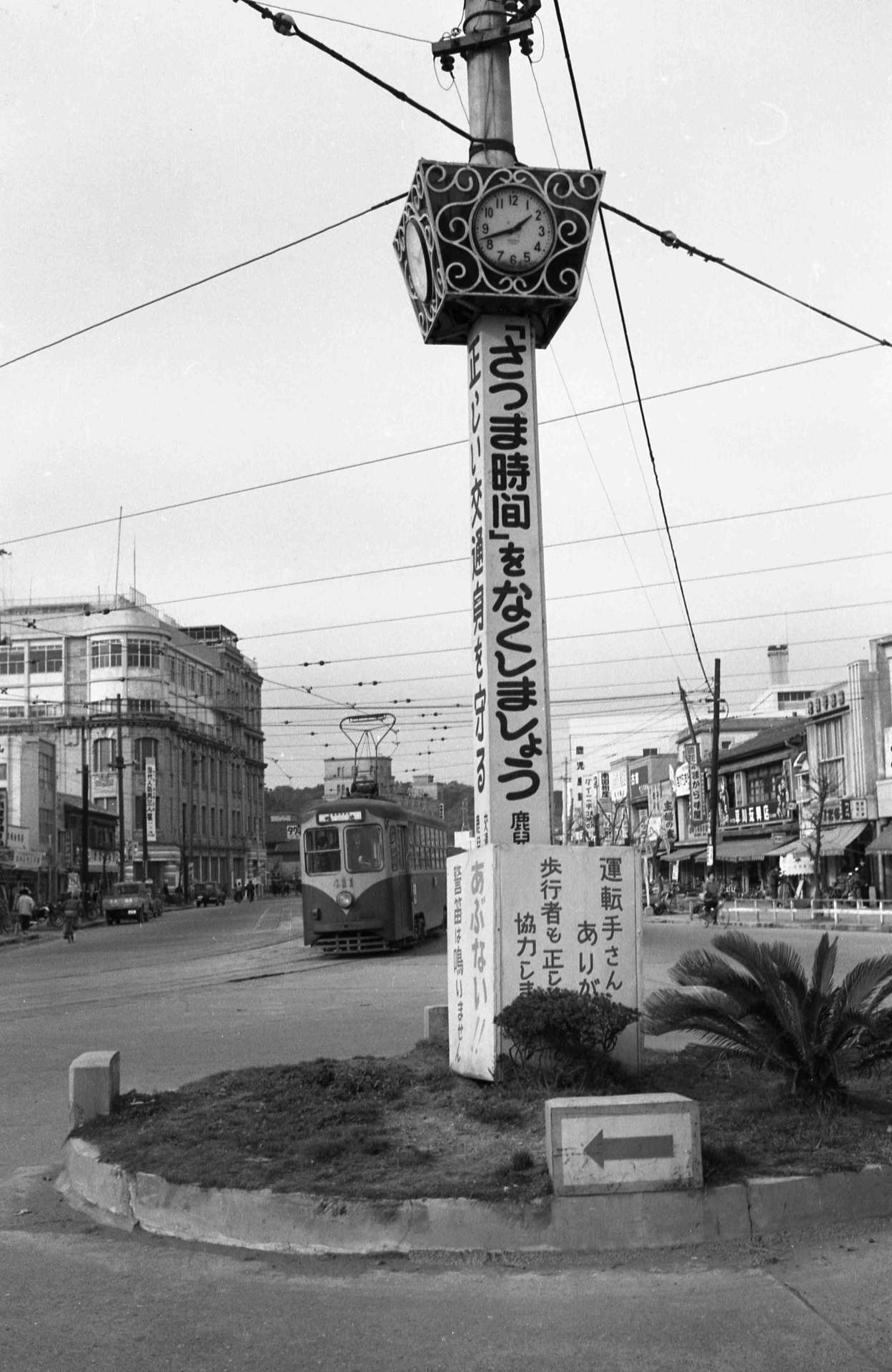 さつま時間鹿児島市の繁華街「いづろ交差点」に立つ時計塔。「『さつま時間』をなくしましょう」と大書してある＝１９６０年２月１日、鹿児島市大黒町のいづろ交差点