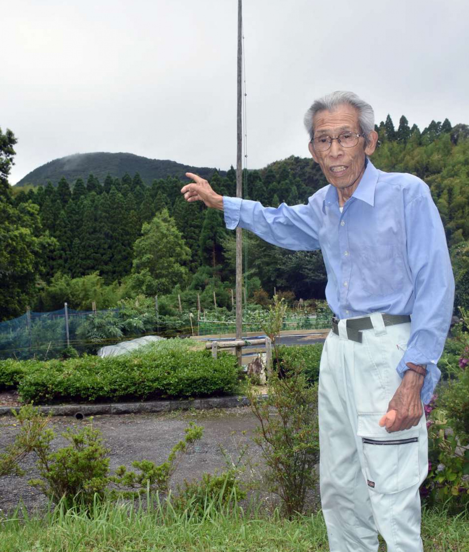 上床山の方角を指し、戦時下の様子を振り返る折橋義行さん＝阿久根市山下