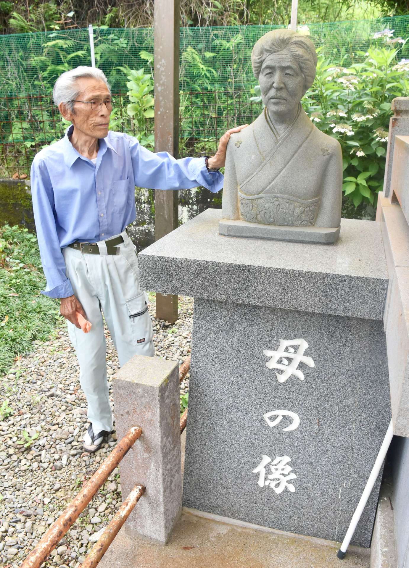 庭に飾る実母の銅像を見ると、戦争時代を思い出すという折橋義行さん＝６月２３日、阿久根市山下