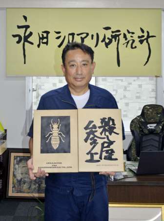 シロアリの看板とキャッチコピーの原版を手にほほ笑む永田シロアリの永田公宏社長＝鹿児島市照国町