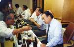 京都県人会に参加し、稲盛和夫さん（右から２人目）の隣で杯を交わす鶴丸明人さん（右）＝１９９９年７月（鶴丸さん提供）