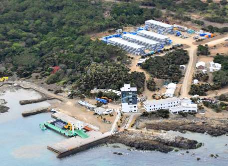 【別カット】重機や資材を積んだ台船が接岸し、工事の準備が進む葉山港周辺。上は新設された作業員用宿舎＝１２日午後２時半、西之表市の馬毛島（本社チャーター機から撮影）