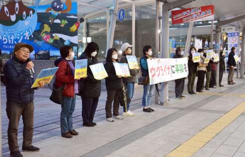 横断幕やプラカードを手に戦争終結を訴える人たち＝２４日、鹿児島市中央町のＪＲ鹿児島中央駅前