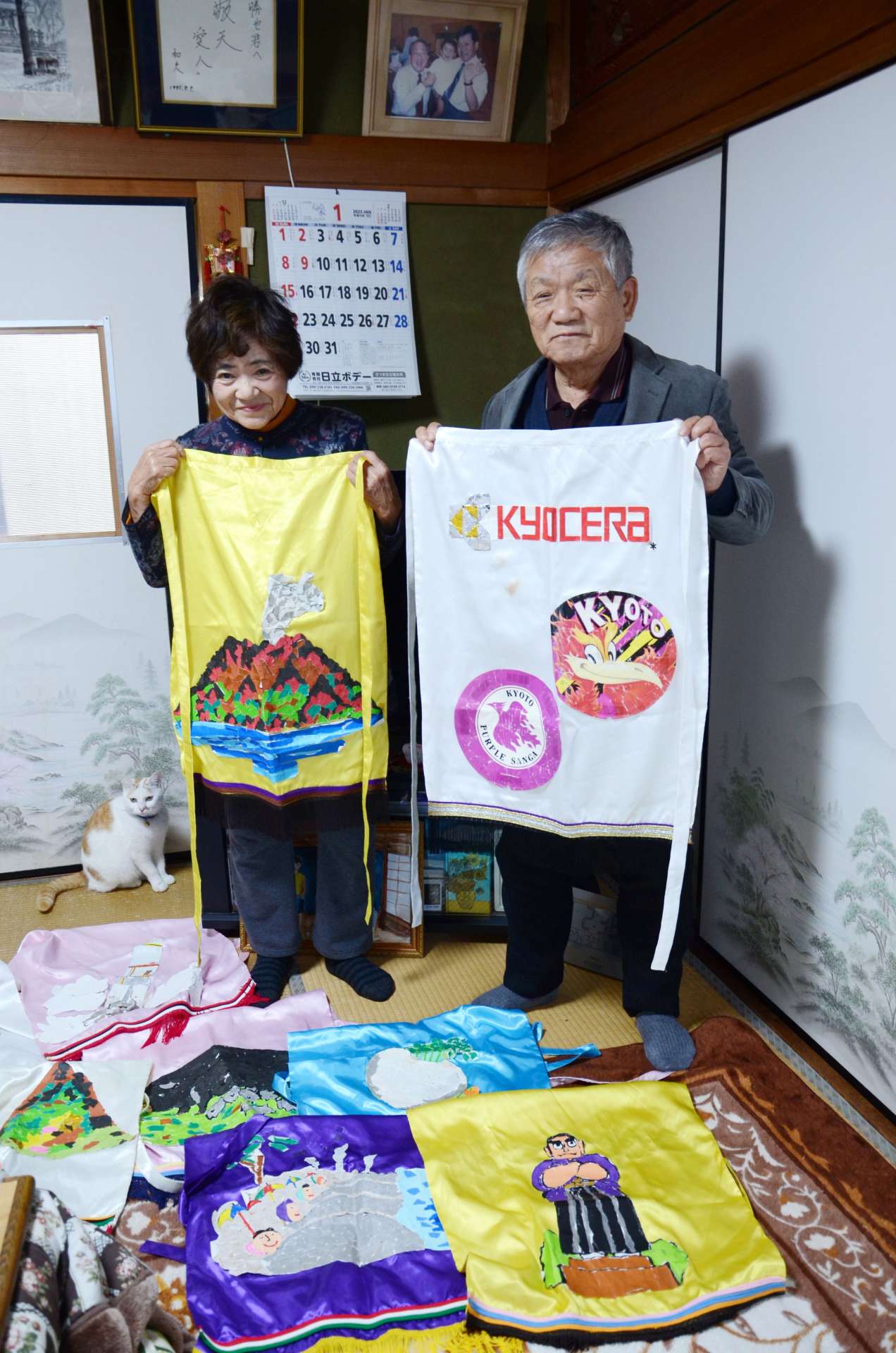 「稲盛会」で披露する相撲踊りのため手作りした化粧まわしを持つ稲盛勝也さん、たづ子さん夫妻＝鹿児島市小山田町