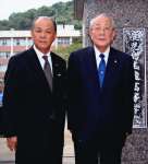 母校の前で記念撮影する渕本逸雄さん（左）と稲盛和夫さん＝２０１４年１０月、鹿児島市の鹿児島玉龍高校