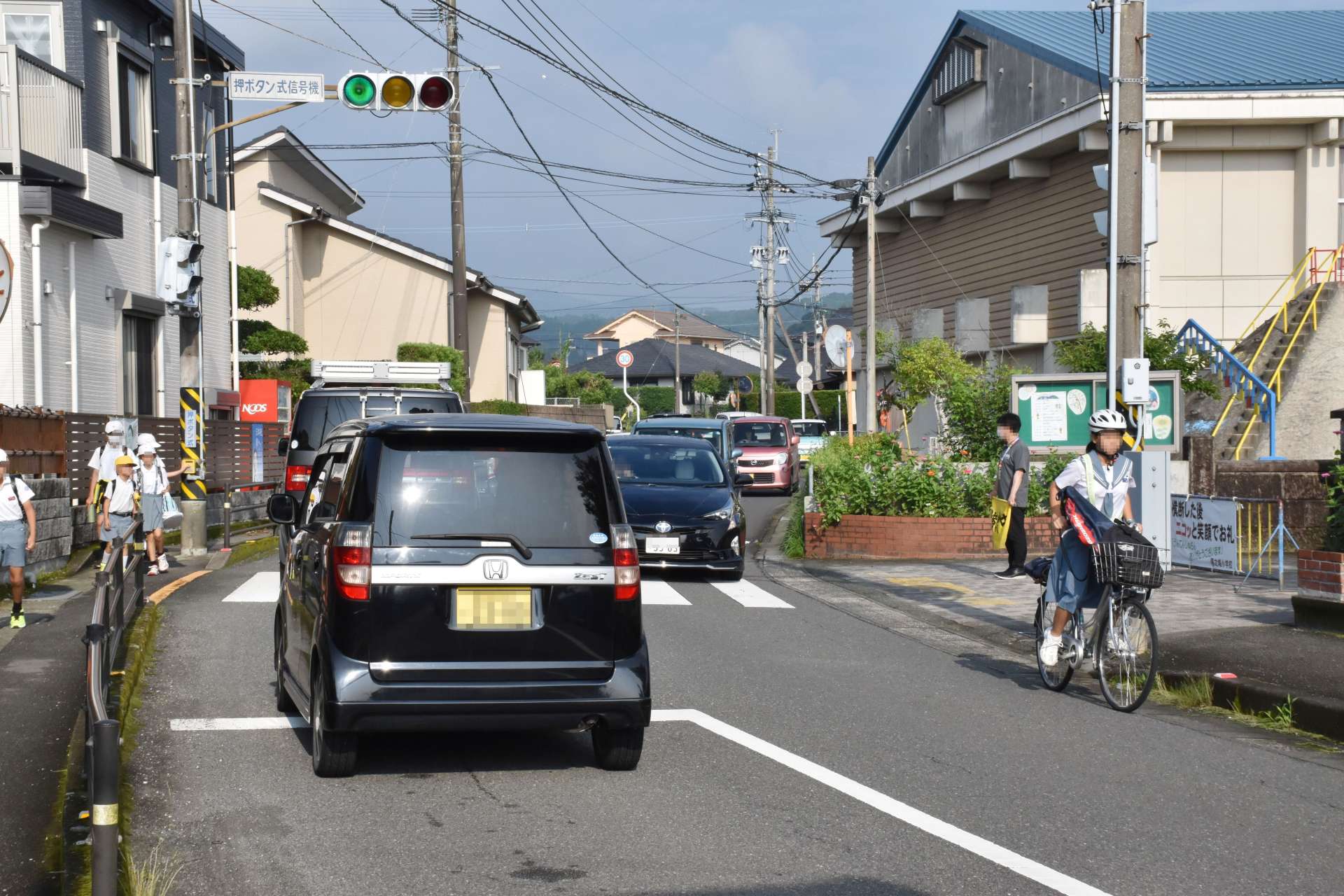 児童の登校時間は、隈之城小学校前の道路を多くの車や自転車が通行する（画像の一部を加工しています）＝６日午前７時４５分すぎ、薩摩川内市隈之城町