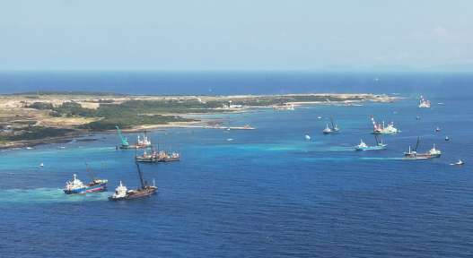 砂利などの投入で海中に帯のような筋が伸びる島の南東部＝１０日午前（小型無人機で撮影）