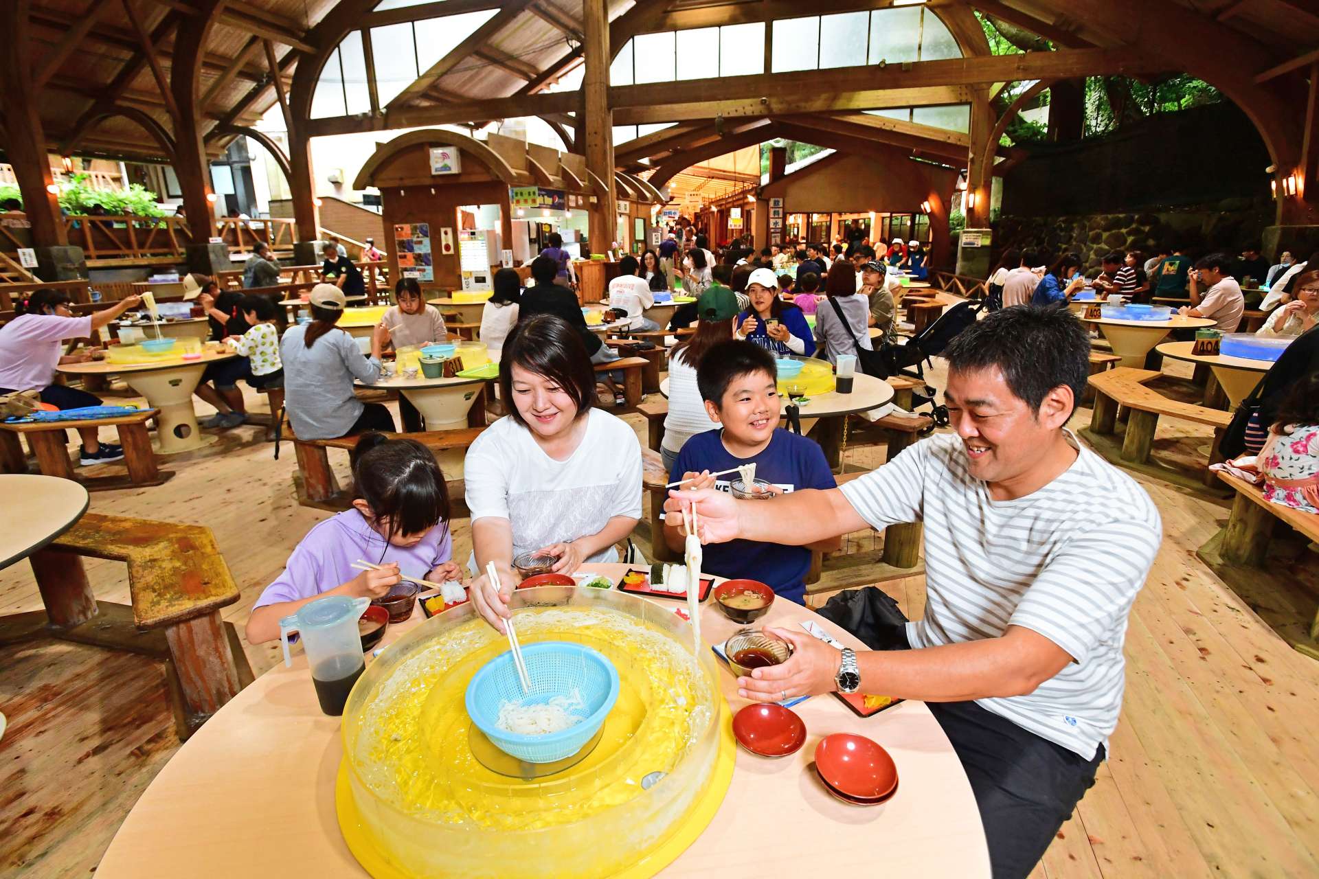 涼しげに流れるそうめんを味わう家族連れ＝指宿市営「唐船峡そうめん流し」