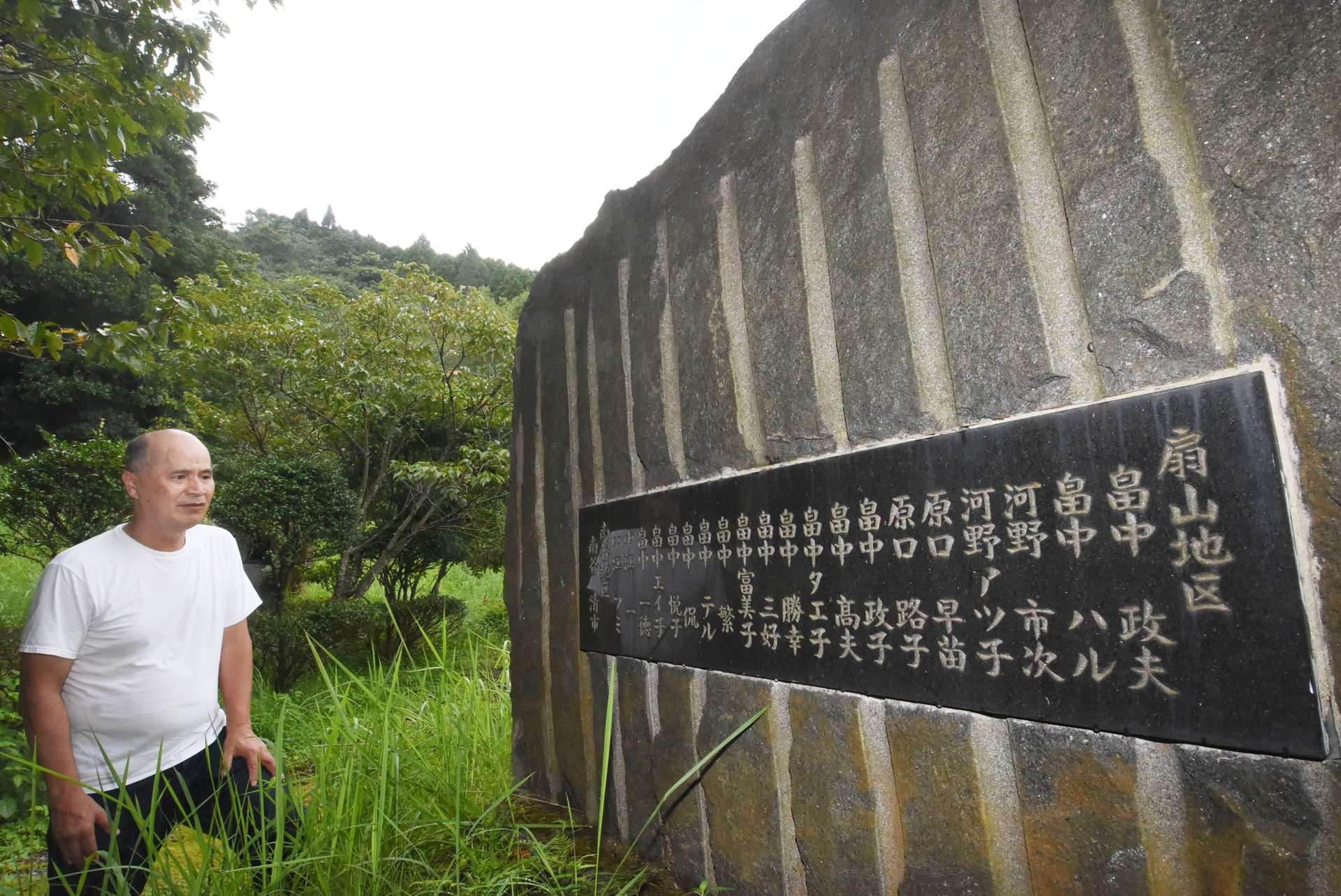 扇山集落の犠牲者２０人の名前が記された慰霊碑を見つめる畠中博文自治会長＝南さつま市金峰町大坂の扇山公園