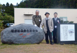 ２０２１年１２月、コガネセンガンの生みの親をたたえる顕彰碑の横に立つ坂井健吉さん（中央）＝鹿屋市