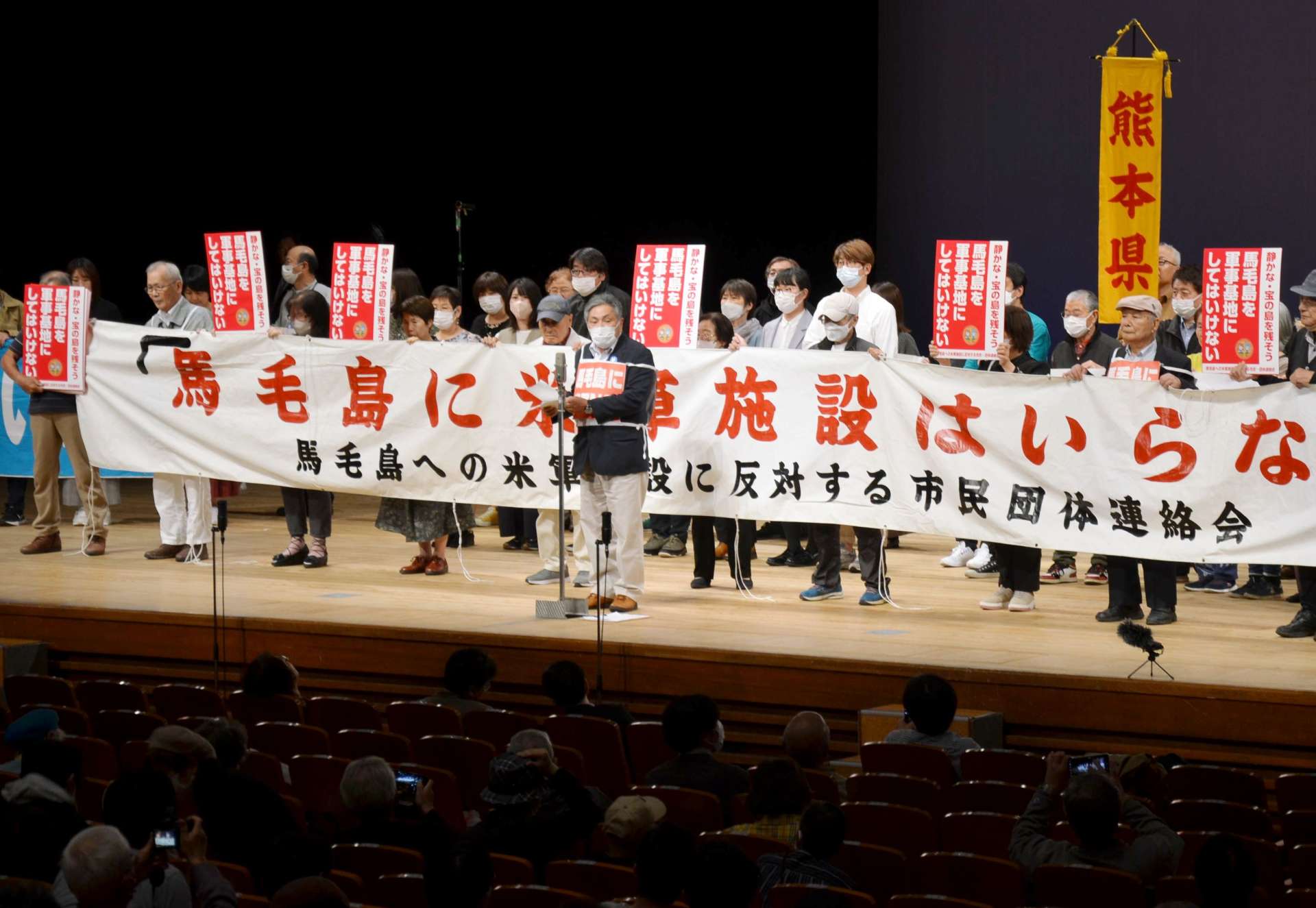 「馬毛島に軍事基地はいらない」と訴える山内光典会長（中央）＝１１日、鹿児島市の宝山ホール