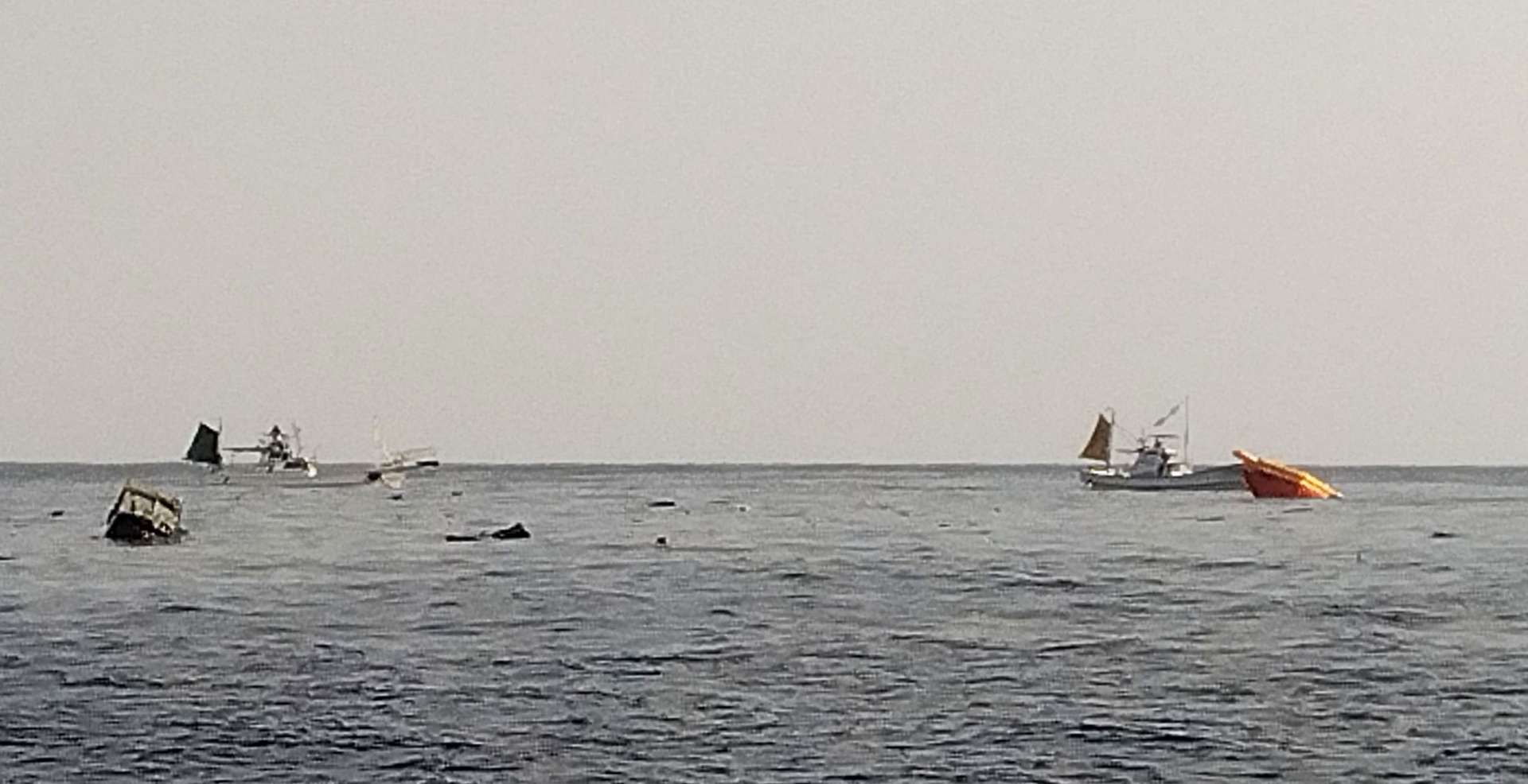 海面を漂う機体の一部とみられる残骸と救助活動にあたる漁船＝２９日午後３時ごろ、屋久島沖（提供写真）