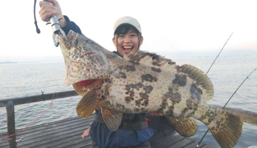 釣り仲間が釣った６キロのチャイロマルハタを持って気合が入る＝１１月４日午前、桜島沖