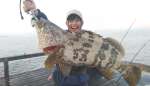 釣り仲間が釣った６キロのチャイロマルハタを持って気合が入る＝１１月４日午前、桜島沖