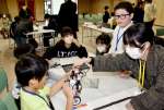鹿児島高専の鎌田鈴音さん（右）からロボットのプログラミングを学ぶ子供たち＝垂水市市民館