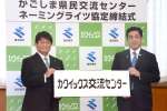「カクイックス交流センター」と書かれたパネルを手にするカクイックスの岩元文雄社長（左）と塩田康一知事＝１３日、県庁