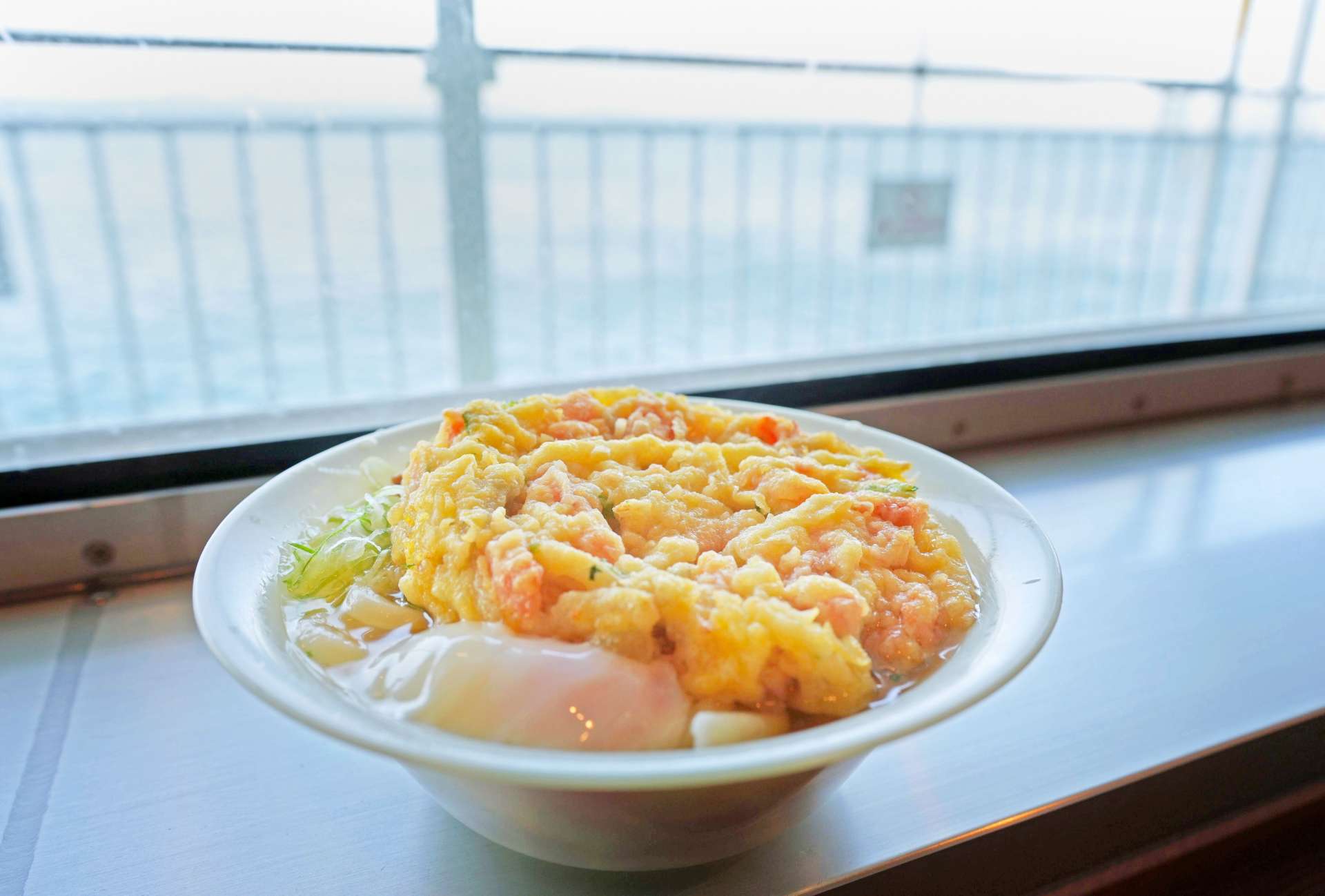 かきあげと温泉卵がのった月見かきあげうどん。窓際のカウンター席では景色を楽しみながら食べられる＝鴨池・垂水フェリー船内