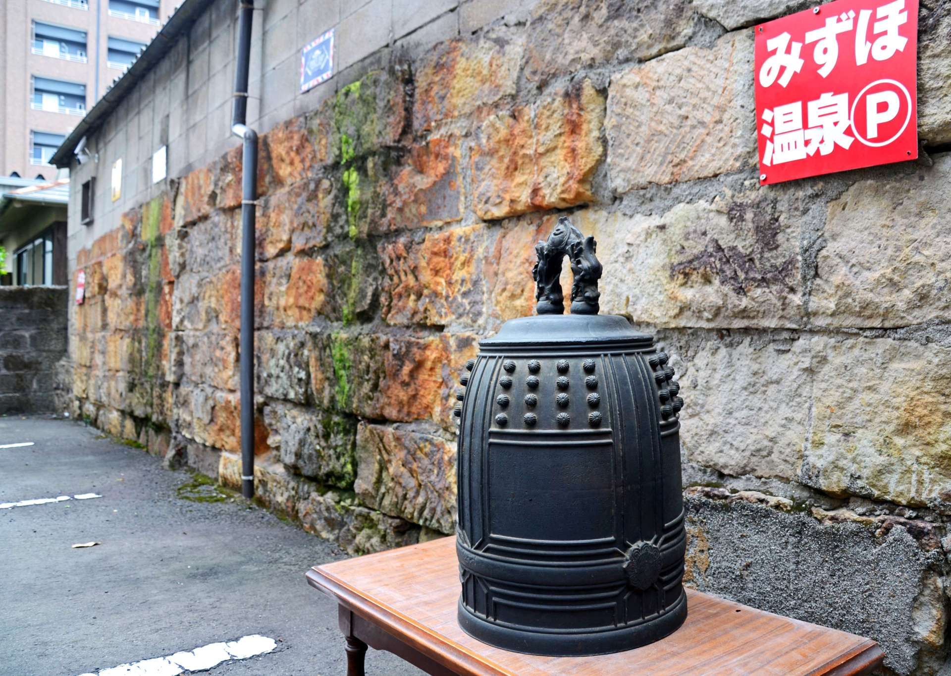 焼夷弾による火災で、赤黒く焼けた石を積んだ塀が戦禍の記憶を伝える。空襲の夜に打ち鳴らされた消防団の半鐘は、望楼の焼け跡で見つかった＝鹿児島市上荒田町のみずほ温泉