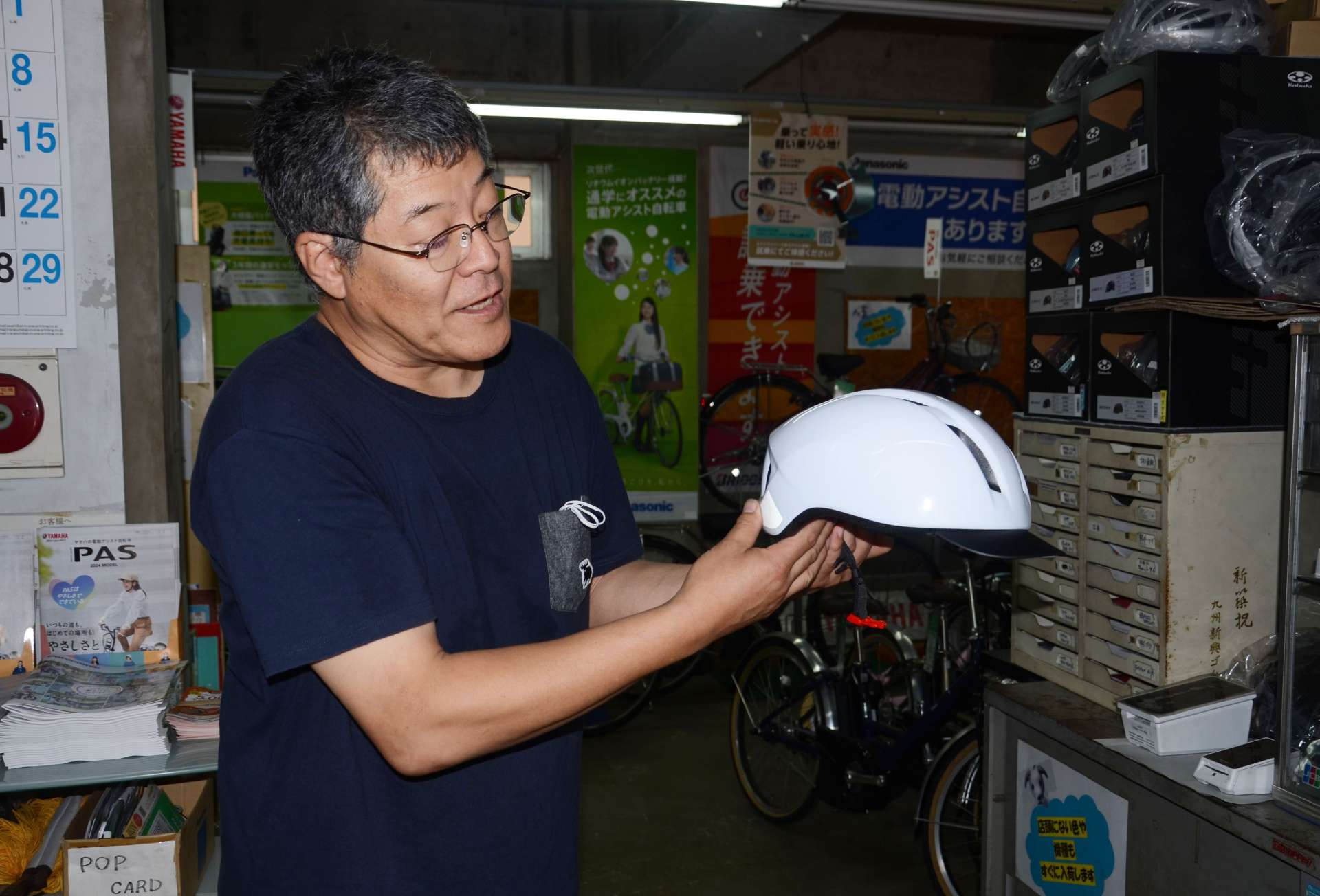 つば付きヘルメットを説明する冨ケ原多聞店長＝鹿児島市平之町のじてんしゃのトミハラ