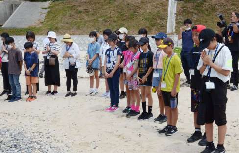 遺体が流れ着いた海岸で黙とうをささげる沖縄の児童＝１４日、宇検村の船越海岸