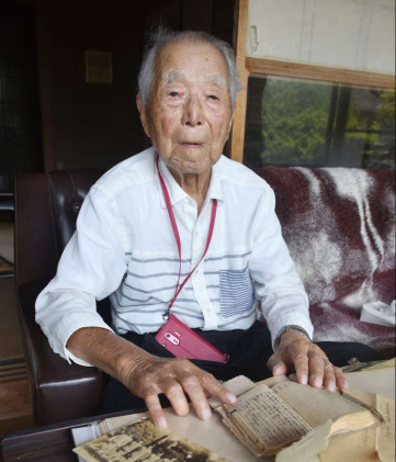 戦時中の写真など資料を前に語る吉ケ別符利夫さん＝鹿屋市上野町