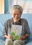 〈別カット〉作品集「結の花」を手に笑う廣島員代さん＝伊仙町木之香