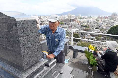 お供え用の花を用意し、墓石を磨く夫婦＝１９日、鹿児島市の郡元墓地