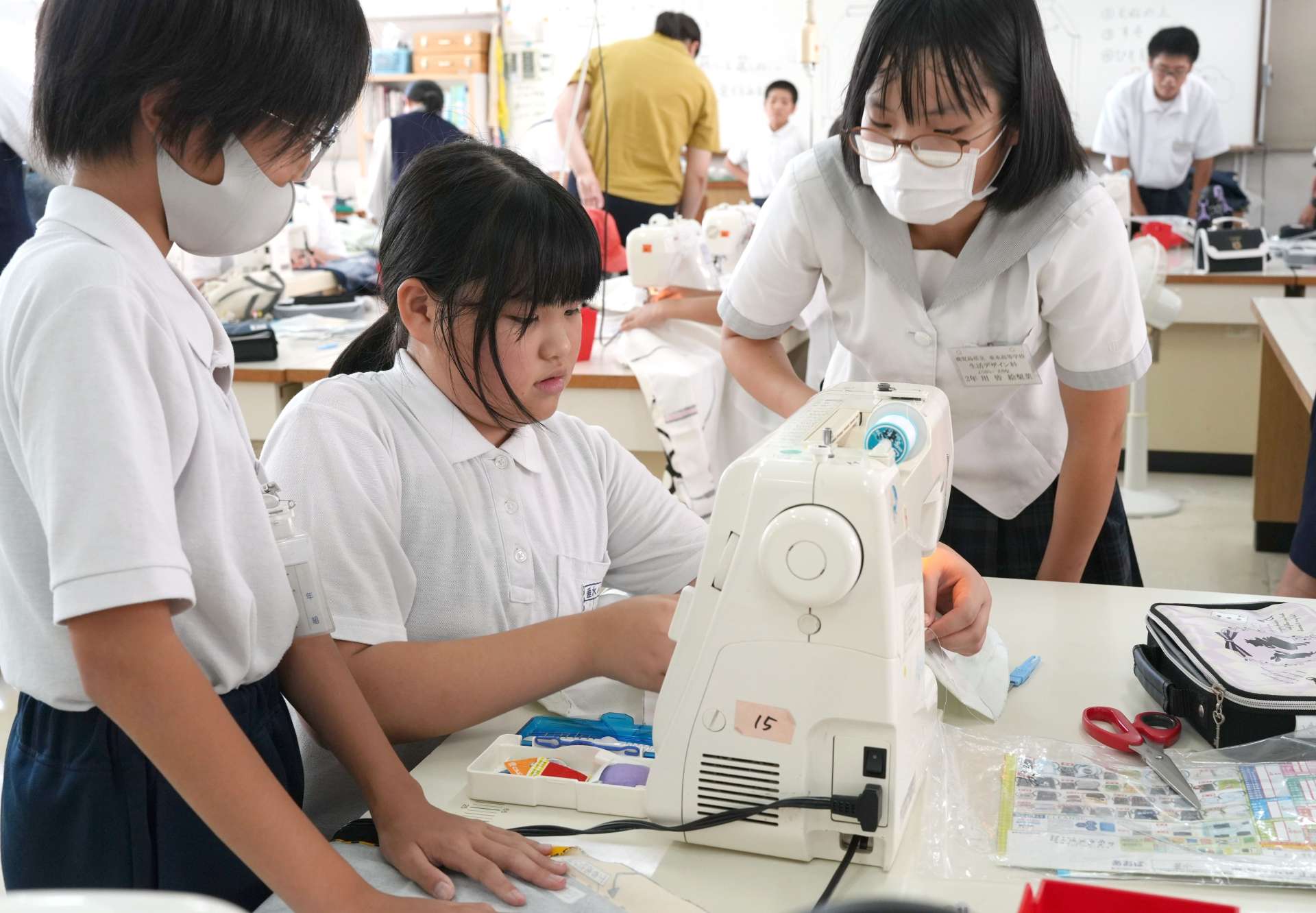 高校生（右）の指導を受けながらミシンを操作する小学生＝垂水市の垂水高校