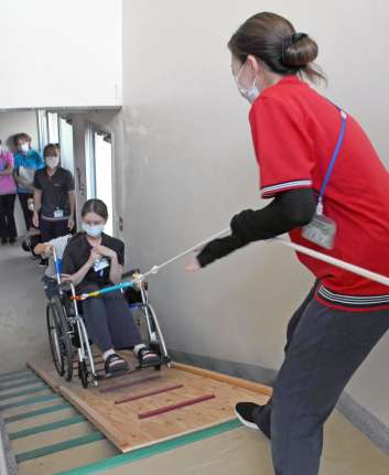 避難用スロープでロープを使い、車いすを引き上げる職員＝志布志市有明のありあけ苑