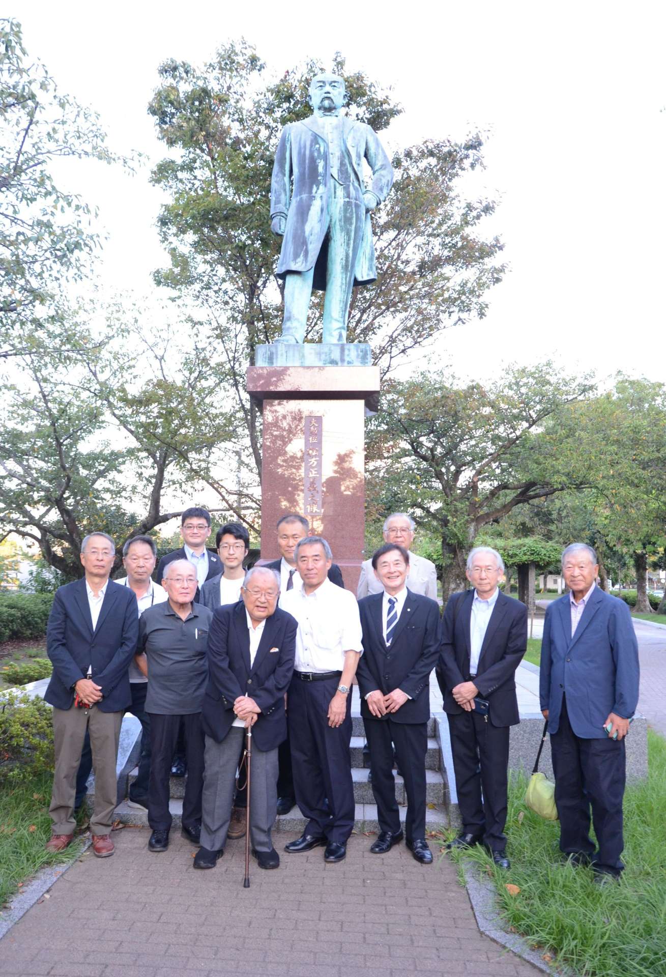 孫の松方峰雄さん（手前）を囲む没後１００年実行委員会のメンバー＝鹿児島市甲突川沿い