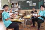 給食を前に、阿久根産の丸干しを手にする児童とイワシ一家のメンバーら＝阿久根市の山下小学校