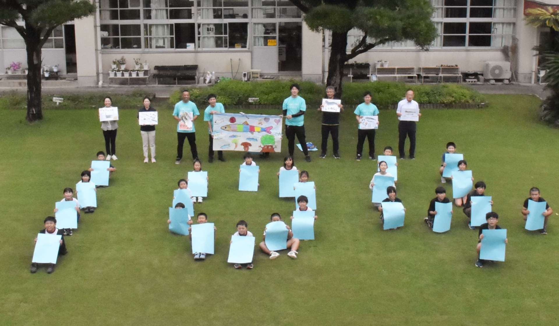 イワシの日を記念して１０４（イワシ）の人文字をつくる山下小の子どもたち＝阿久根市の同校