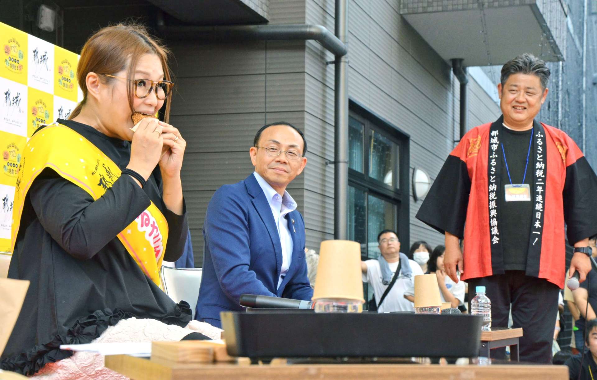 返礼品のメンチカツにかぶりつくギャル曽根さん（左）＝都城市中町